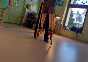 Chętne dzieci z przedszkola "próbują swoich sił" w chodzeniu na szczudłach przy pomocy artysty.